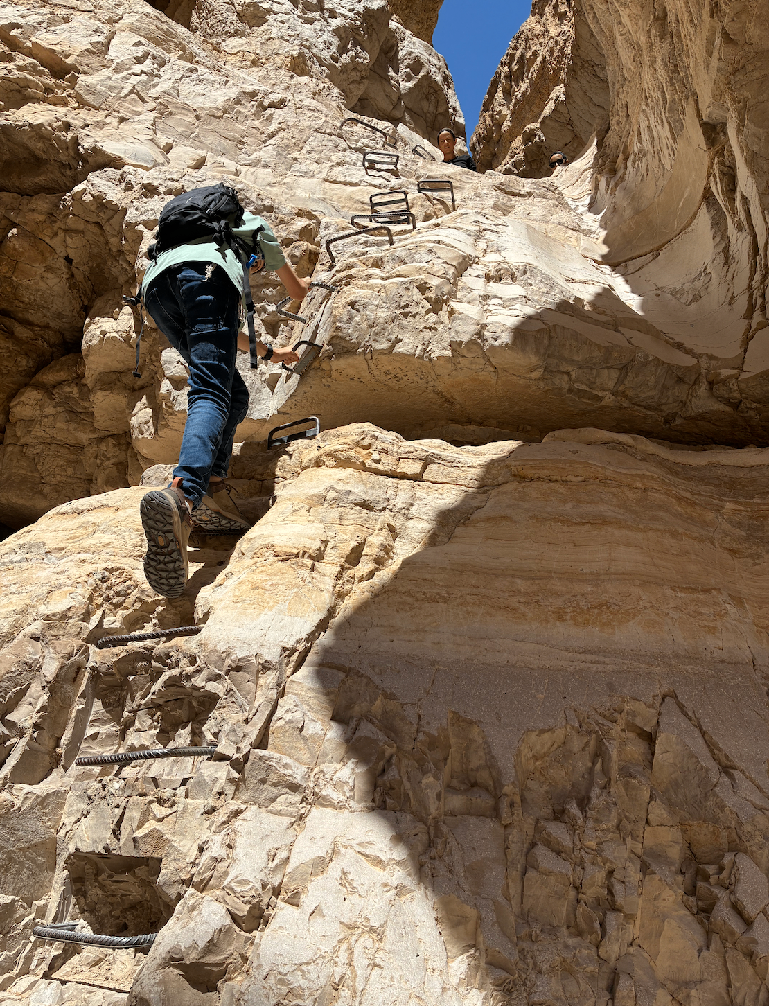 Boy climbing a metal ladder up a sandstone cliff in the Israeli desert